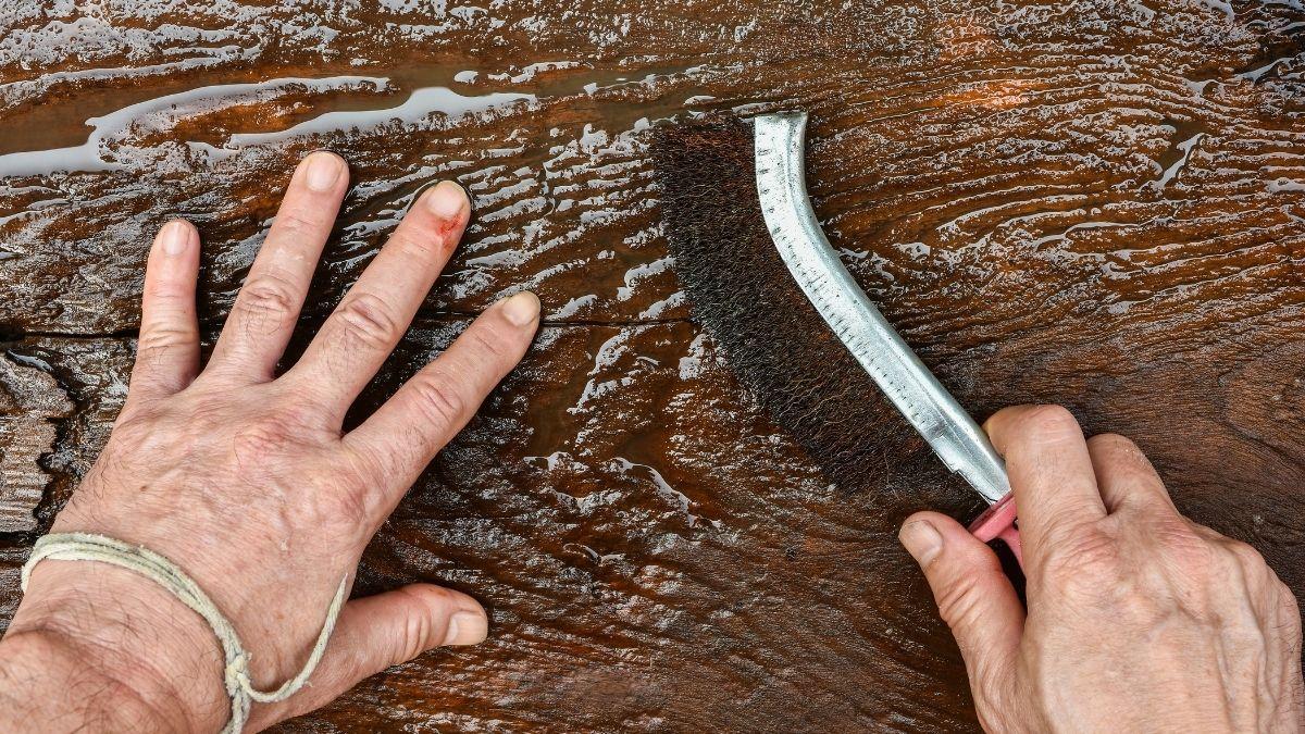 A man holding a brush cleaning a piece of wood