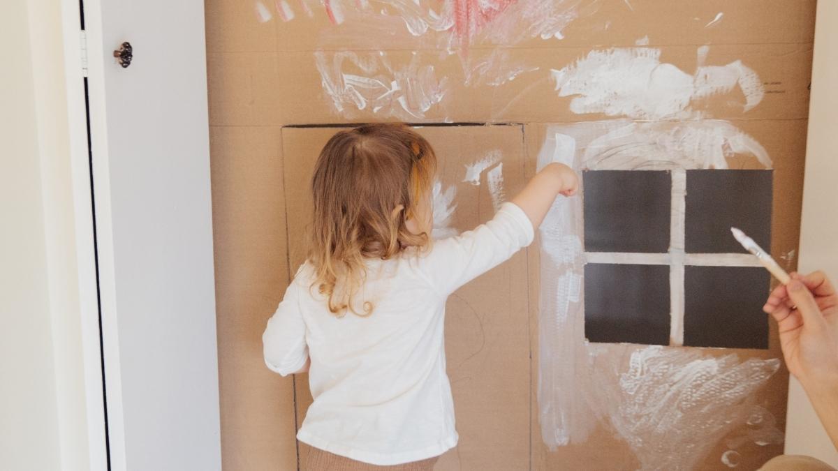 Child painting the cardboard on a box fort