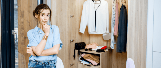 woman looking quizzical standing in front of an open wardrobe of clothes