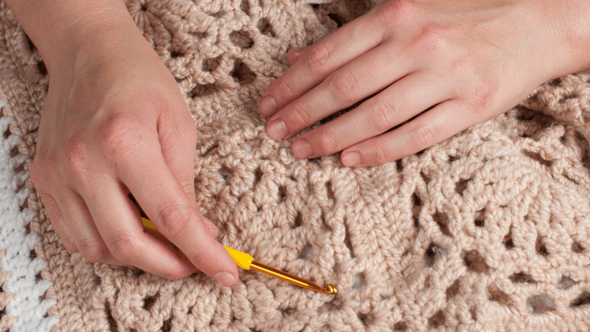 close up of hands holding crochet hook on crochet blanket